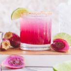 A hot pink cocktail in a glass topped with a lime wedge garnish