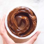 a hand holding a white bowl full of chocolate avocado pudding