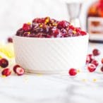 White cup full of cooked cranberries with a brown bottle and jigger in the background