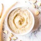 Overhead shot of a white bowl full of parsnip mash and parsnips scattered around